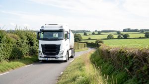 Poids lourd moderne roulant au BioGNV sur une route rurale bordée de haies, sous un ciel lumineux en Bretagne.